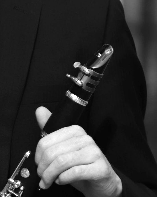 Close-up of a hand holding a clarinet by the barrel, mouthpiece and ligature in view